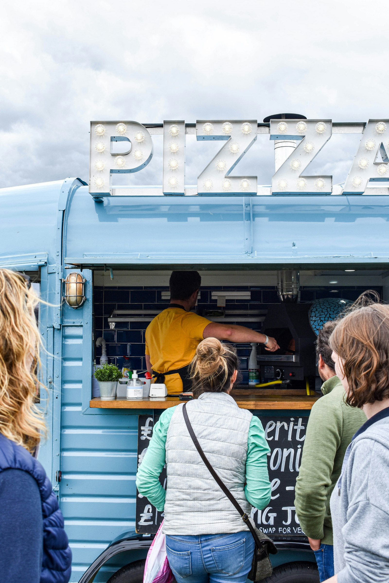 A cook reaching into the oven while customers wait at the service window of a food truck
